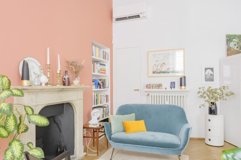 Sala con parete rosa pastello, caminetto e poltrona celeste
