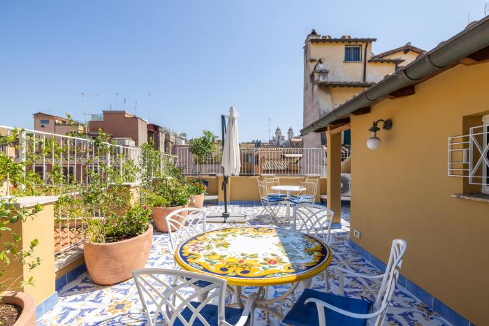Ampia terrazza con pavimento in ceramica decorata, tavolo in maiolica e vista sui tetti di Roma
