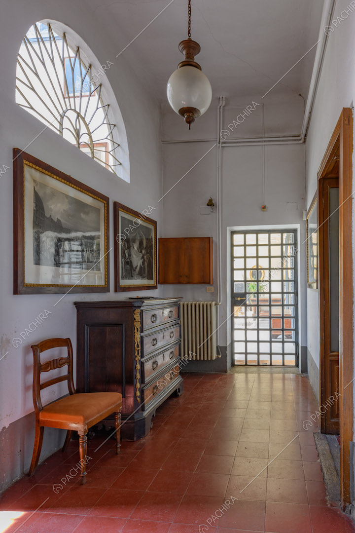 Pavimento in piastrelle rosse, pareti bianche e finestra a mezzo cerchio con decorazione in metallo