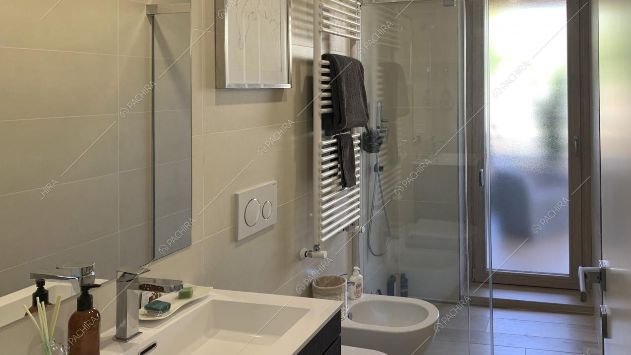 Bagno con piastrelle chiare, radiatore a parete e doccia
