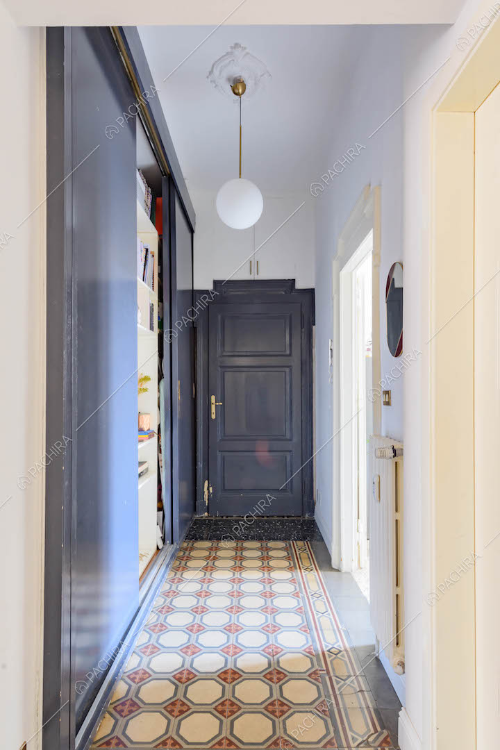 Lungo corridoio con pareti bianche, porta d'ingresso con boiserie e pavimento in graniglia