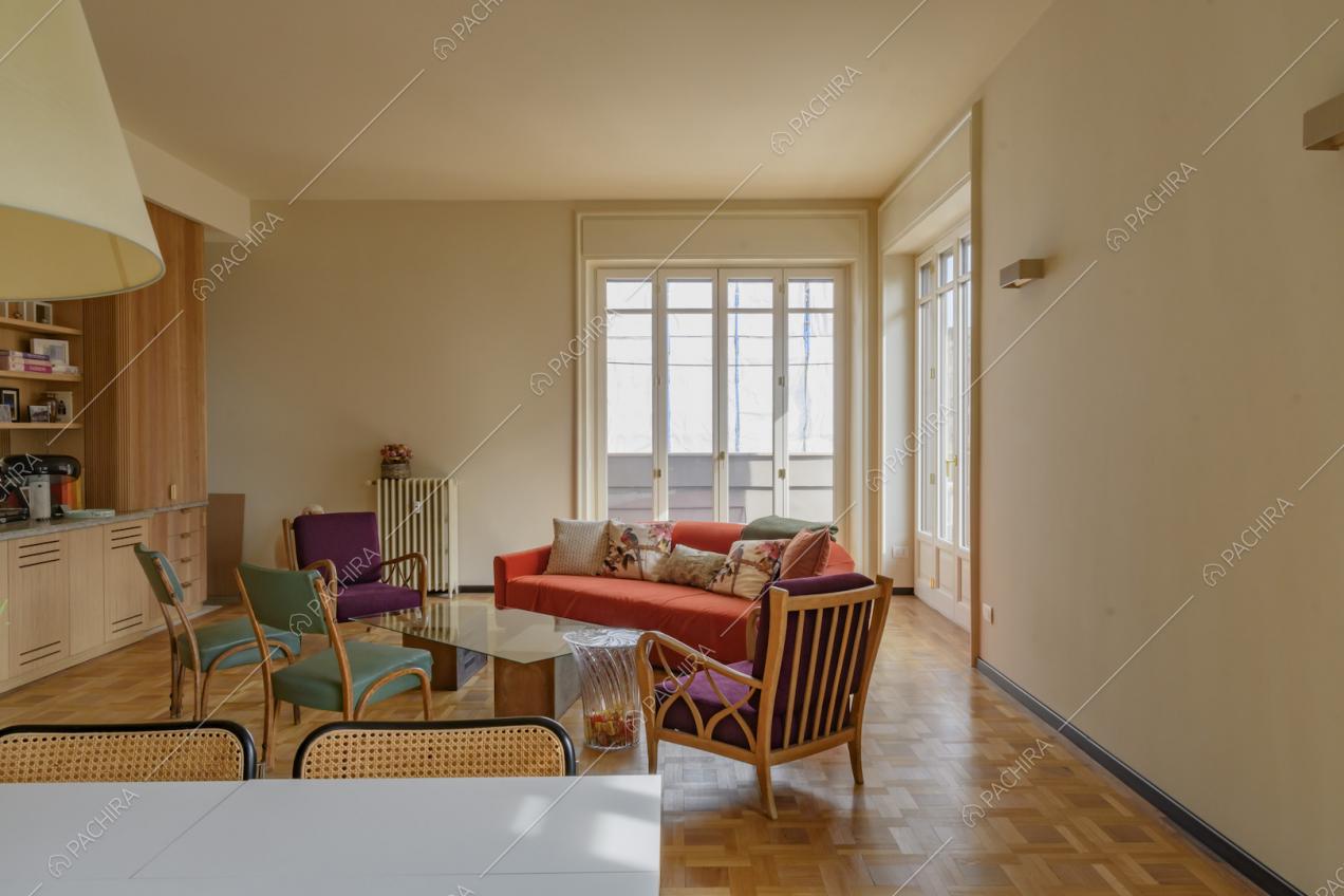 Dal tavolo da pranzo bianco vista sul soggiorno con pavimento in parquet e porte-finestre