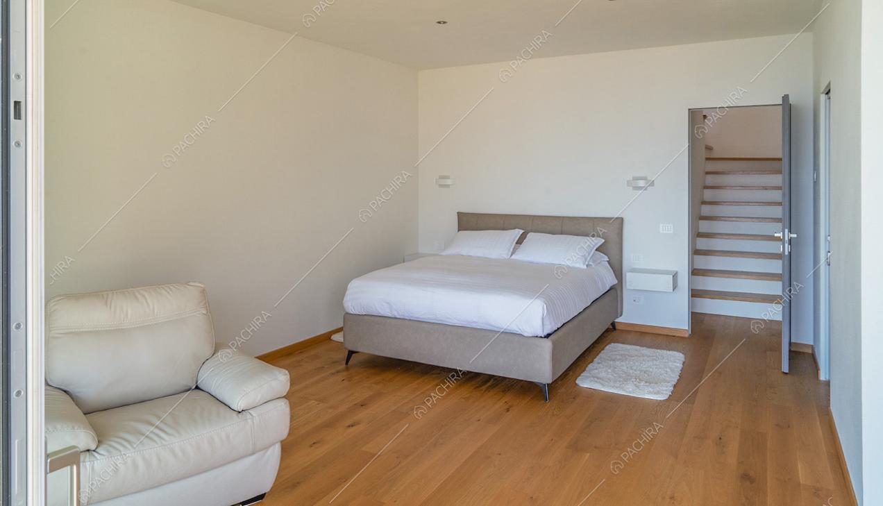 Camera da letto matrimoniale con poltrona bianca, pavimento in parquet, pareti bianche e vista sulle scale