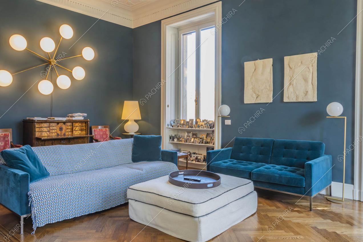 Divani in velluto blu e pouf bianco nel salotto con pavimento in parquet a spina di pesce