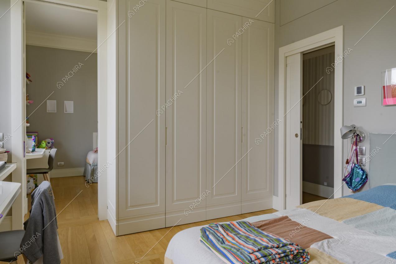 Camera da letto con pavimento in parquet, porta bianca scorrevole e vista su altra camera da letto