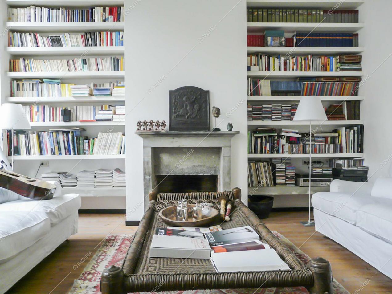 Tavolino nel salotto con libreria a parete, divani bianchi e camino
