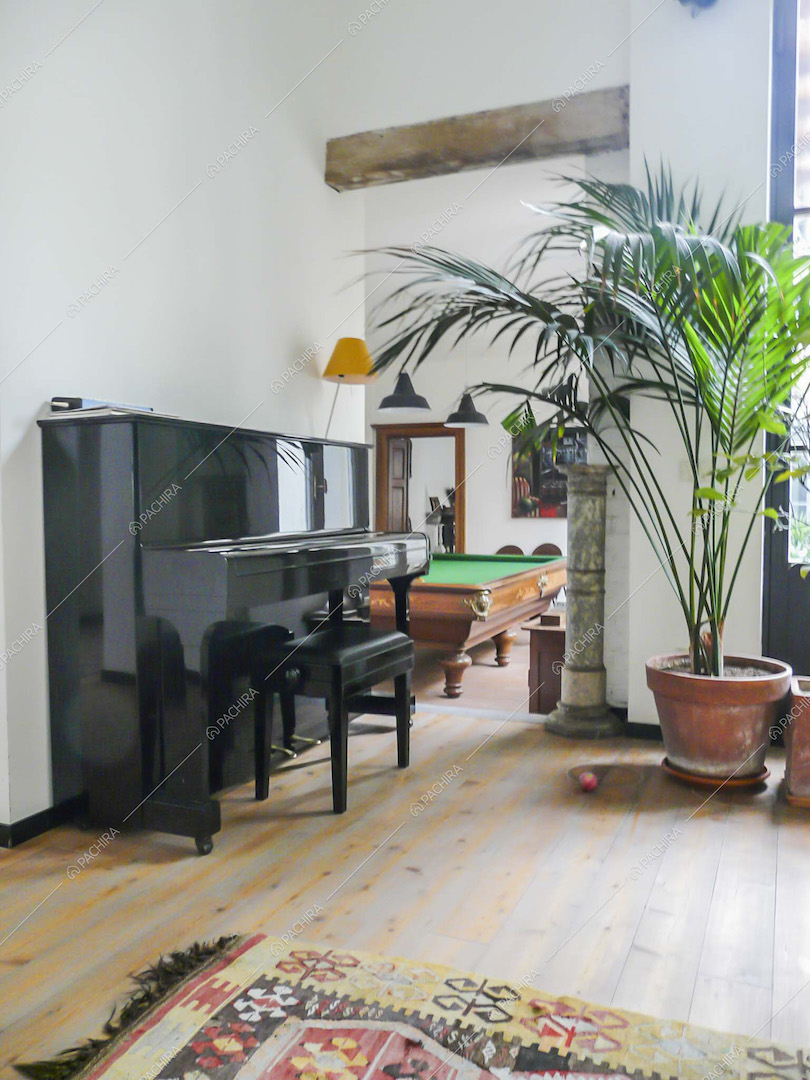 Pianoforte nero a muro e tavolo da biliardo nella sala con pavimento in parquet