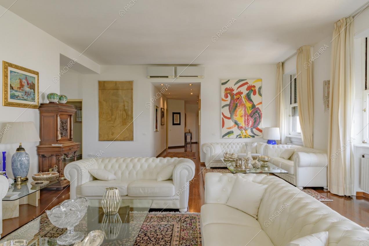 Dai divani in pelle del soggiorno, dalle pareti bianche, vista sul corridoio con pavimento in parquet