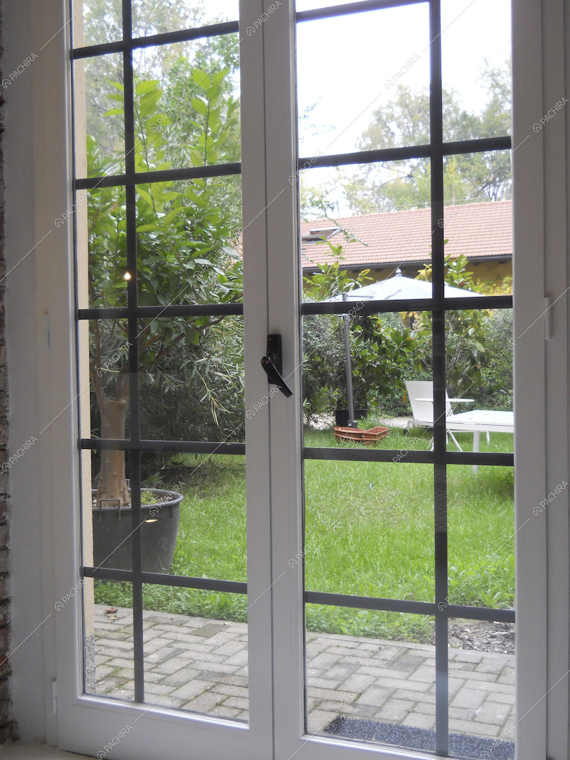 Dalla porta finestra dagli infissi bianchi vista sul giardino con ombrellone