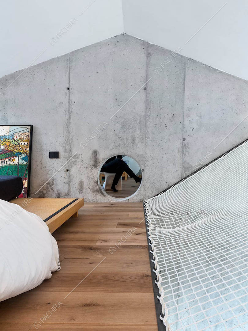 Camera da letto con pavimento in parquet, parete in cemento e rete che funge da ringhiera