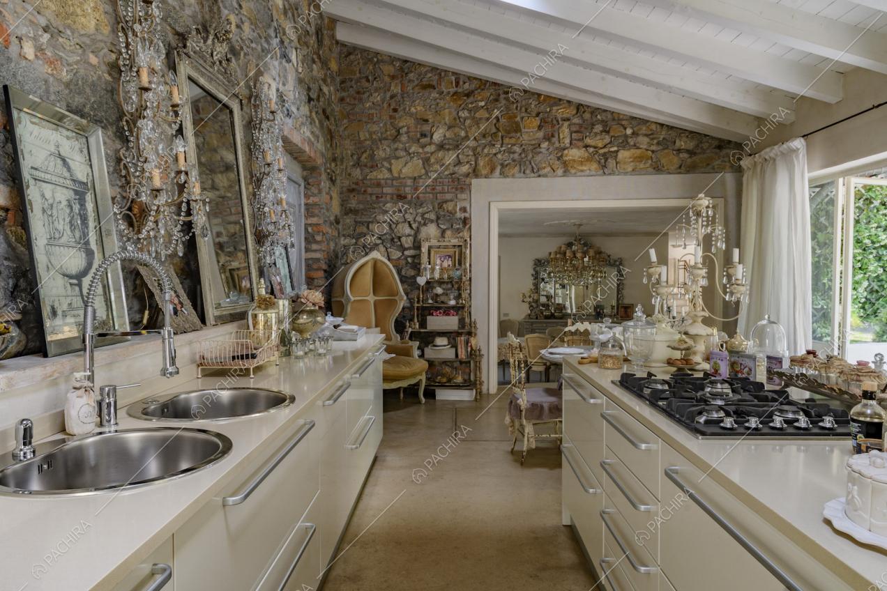 Cucina a vista con isola con fornelli a gas, pareti in pietra e soffitto con travi bianche in legno