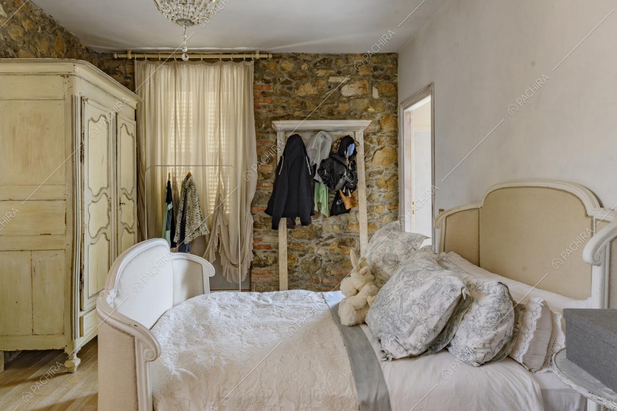 Camera da letto matrimoniale con parete bianca e in pietra e armadio con boiserie