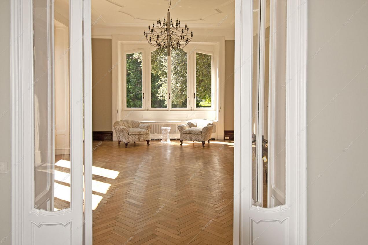 Dalla porta accesso al luminoso salone con pavimento in parquet a spina di pesce, poltrone classiche e lampadario antico