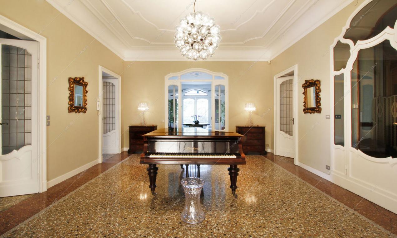 Salone con pianoforte, boiserie sul soffitto e porte classiche dai coprofili bianchi