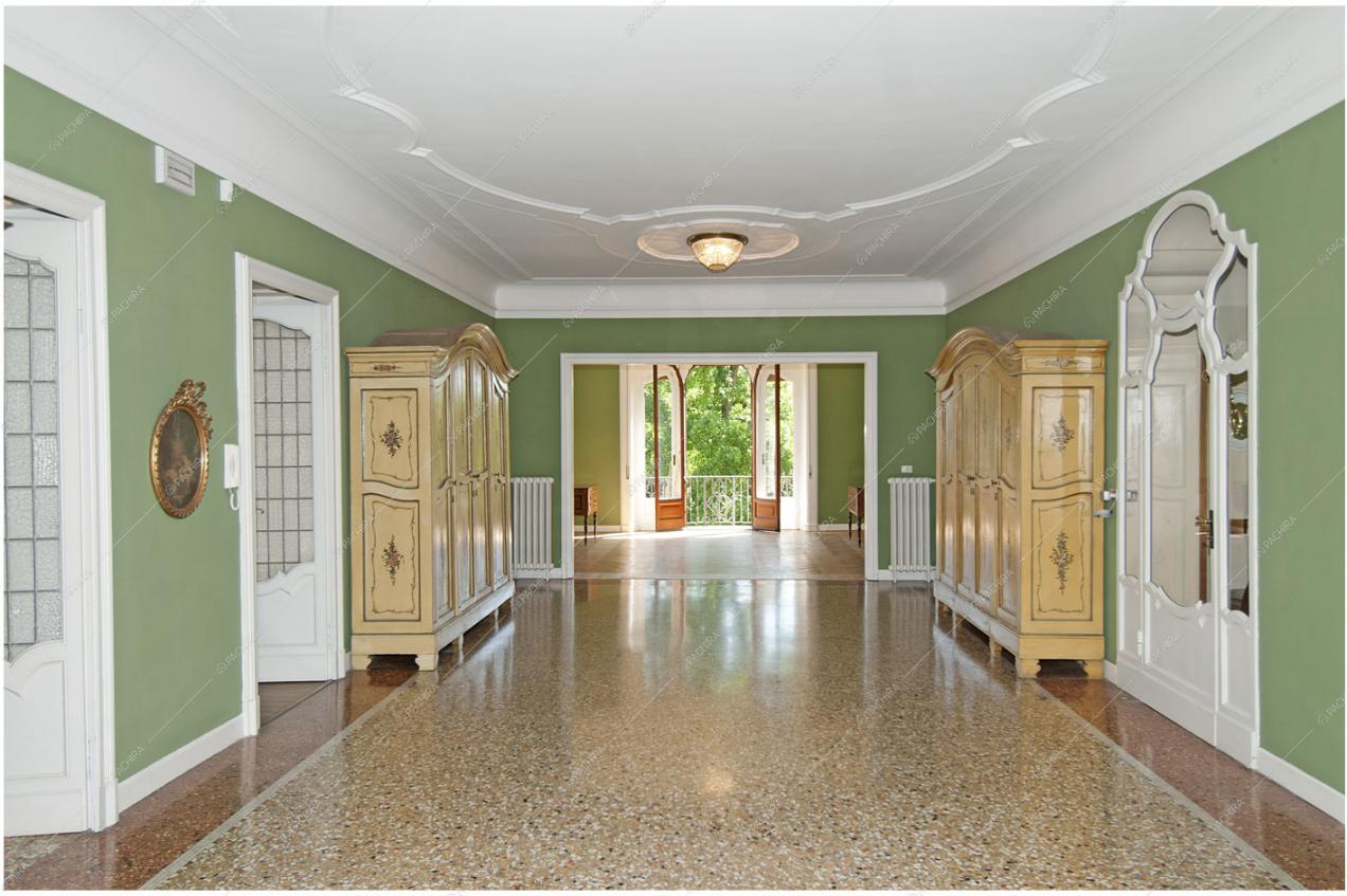 Corridoio dalle pareti verdi, soffitto con boiserie e vista sul balcone con porta-finestra