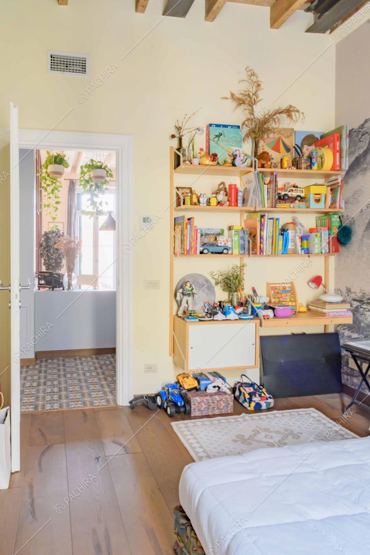 Camera da bambini con pavimento in parquet, pareti gialle e libreria