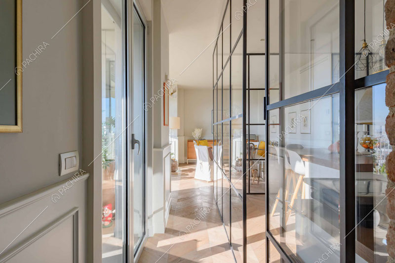 Corridoio con parete grigia e boiserie, pavimento in parquet e parete vetrata industriale