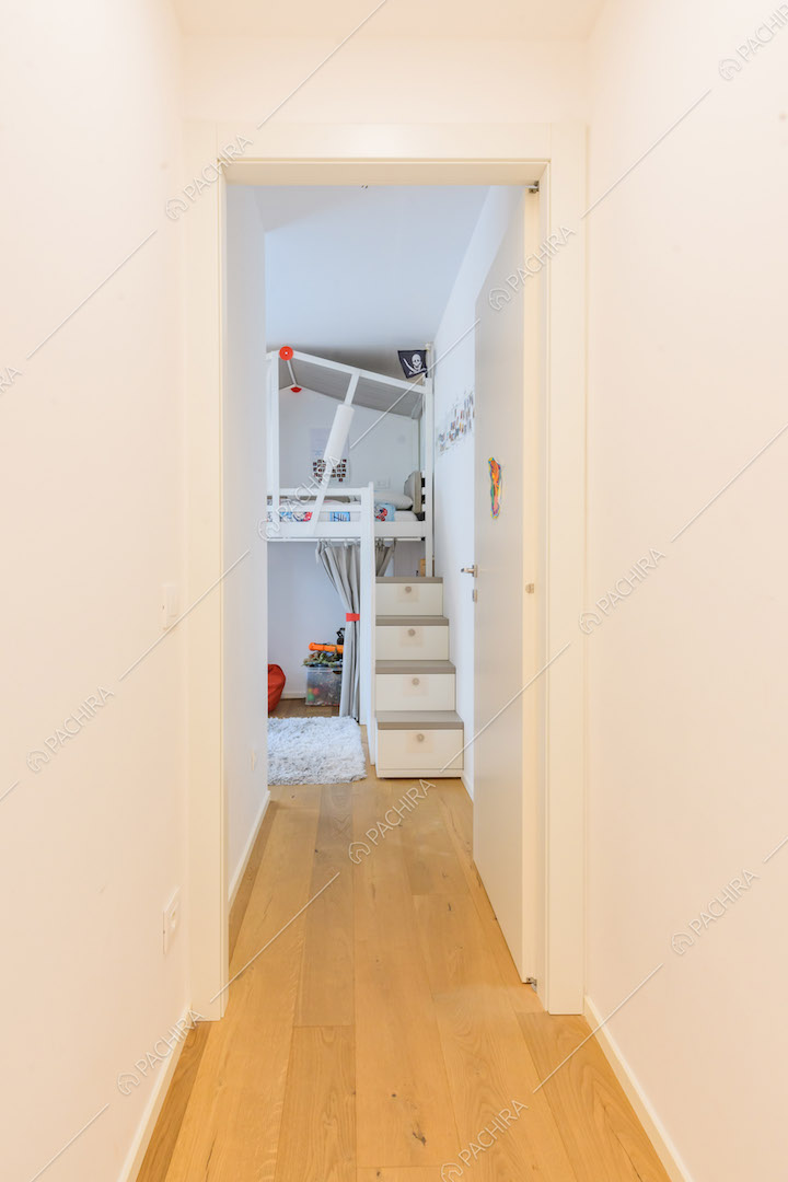 Dal luminoso corridoio con pavimento in parquet e pareti bianche vista sulla camera dei bambini