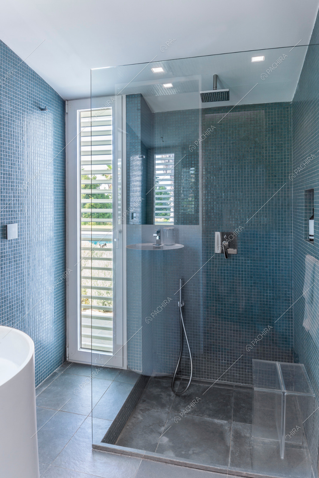 Bagno con box doccia dalla parete in vetro e piastrelle sui muri dai toni blu