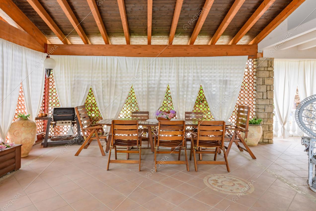 Tavolo da pranzo e sedie in legno nella luminosa veranda con travi a vista