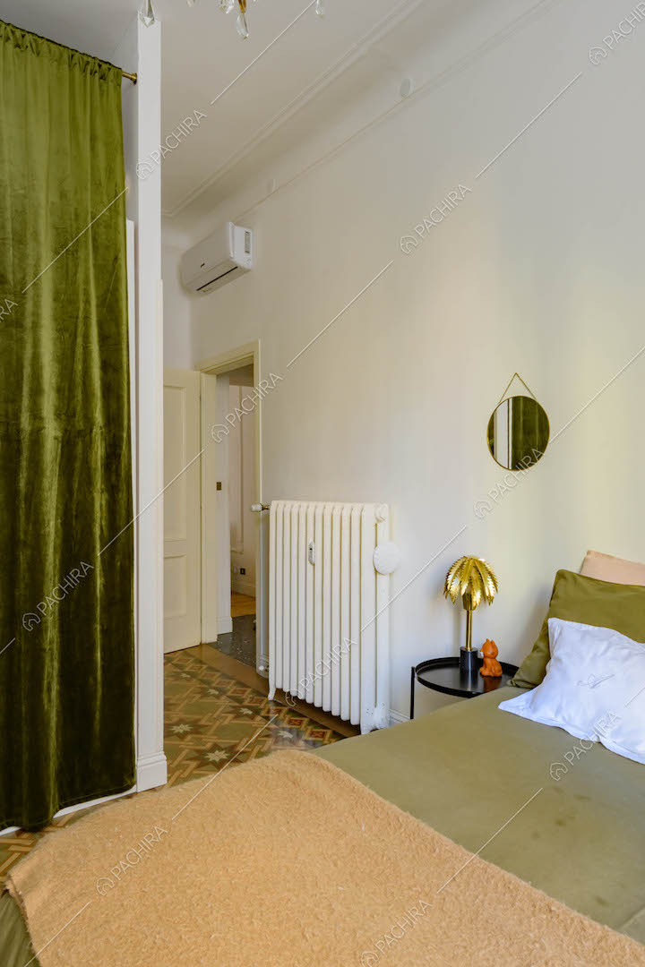 Letto matrimoniale nella camera da letto con pareti bianche e tenda in velluto verde