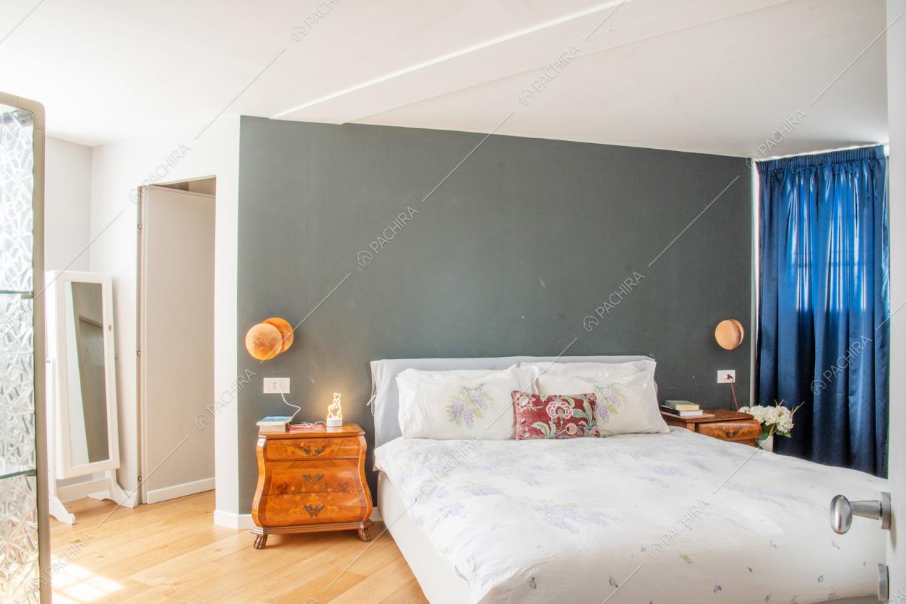 Camera da letto matrimoniale con pavimento in parquet, soffitto bianco e parete grigia