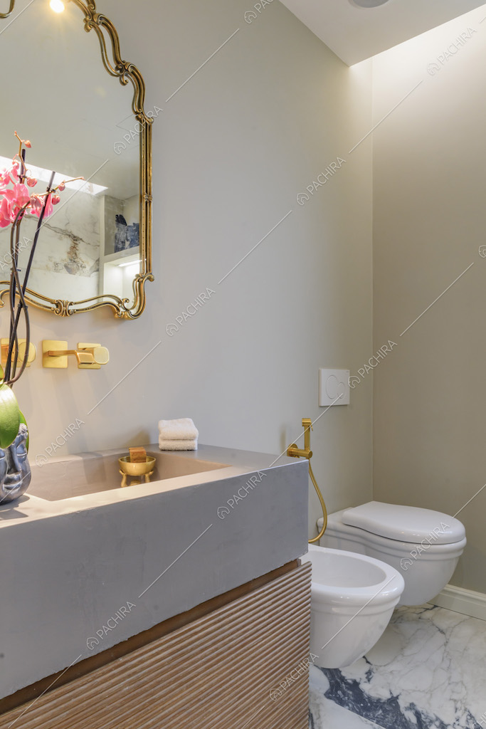 Bagno dal pavimento in marmo con specchio dalla cornice dorata, così come la rubinetteria