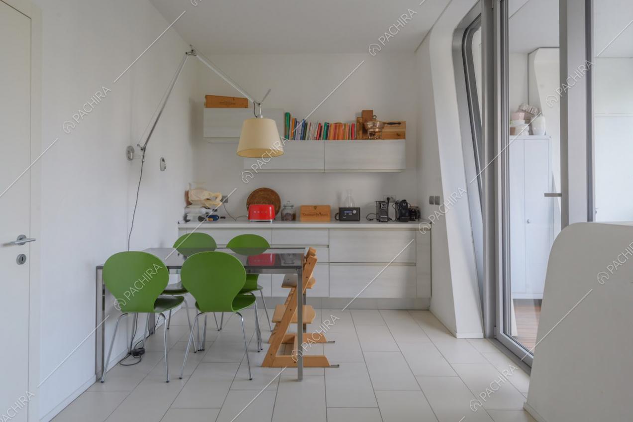 Cucina bianca a parete con tavolo da pranzo nero, sedie verdi e porta-finestra