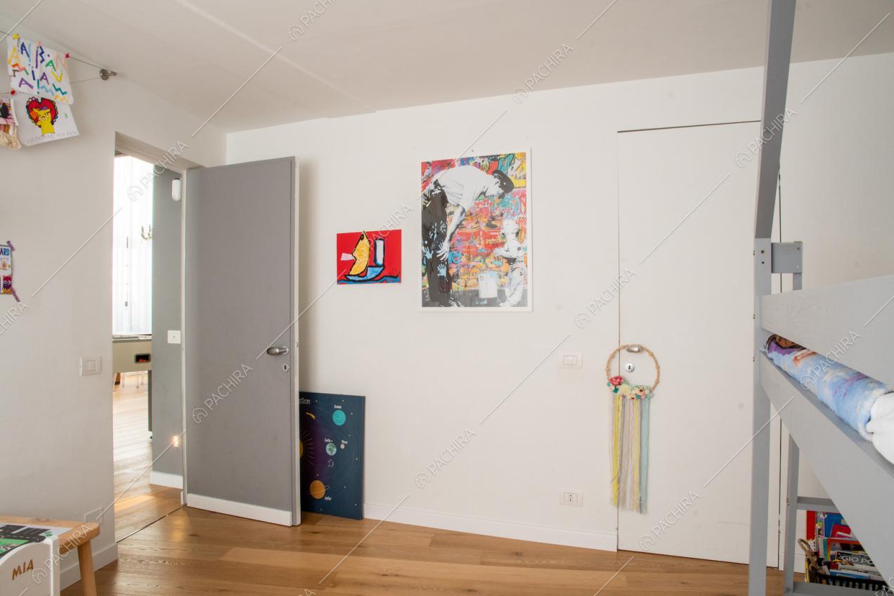 Dalla camera da letto da bambini, con pareti bianche e pavimento in parquet, vista sul soggiorno