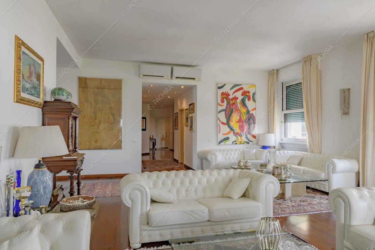 Salotto con pavimento in parquet e pareti bianche, illuminato dalle ampie vetrate