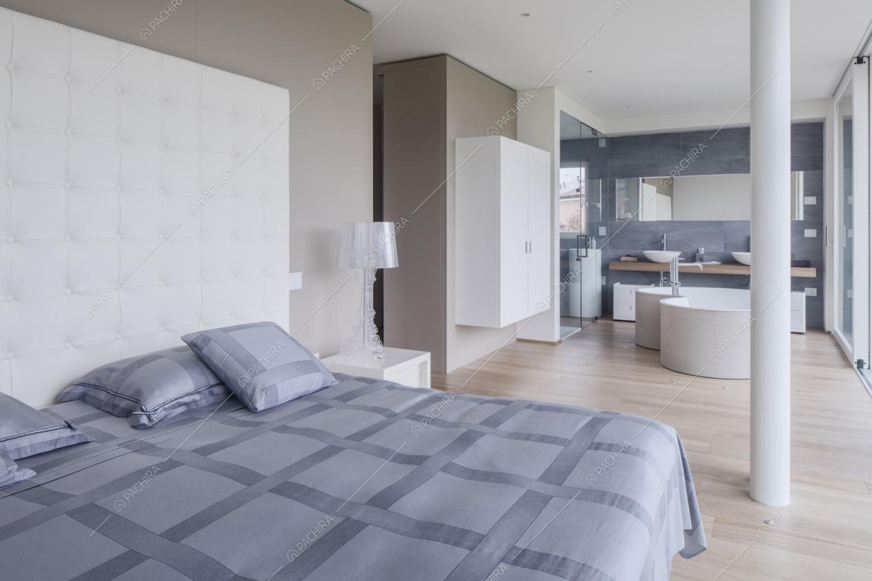 Nella camera dalle pareti beige, letto matrimoniale con testata bianca e vista sulla vasca dalla forma ondulata