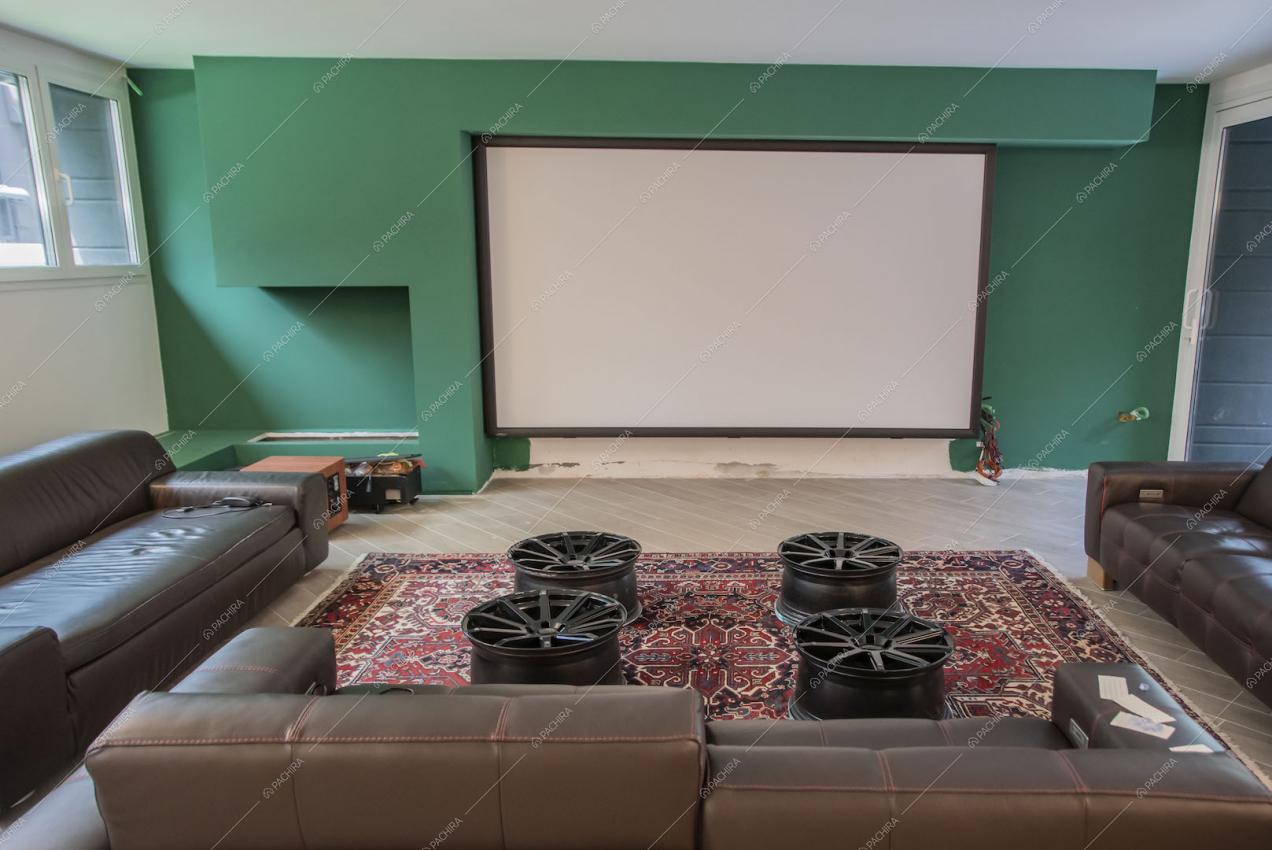 Sala cinema con parete verde scuro, divani marroni in pelle e cerchioni come tavolini