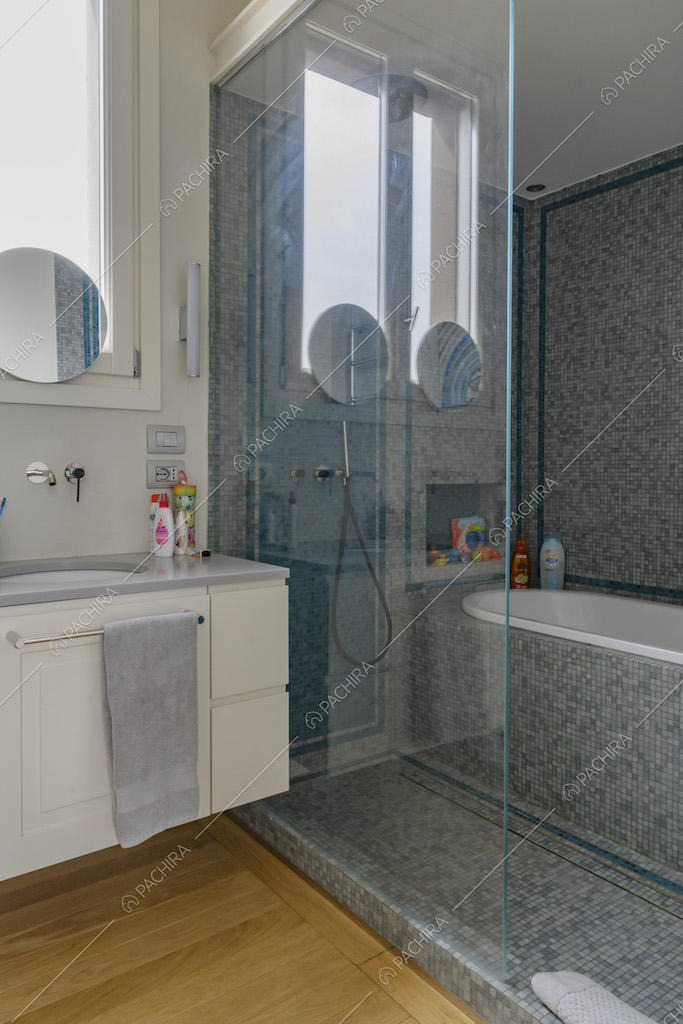 Bagno con pavimento in parquet e vasca separata da una parete in vetro
