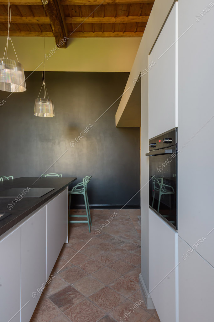 Pavimento in cotto nella luminosa cucina con parete nera e gialla