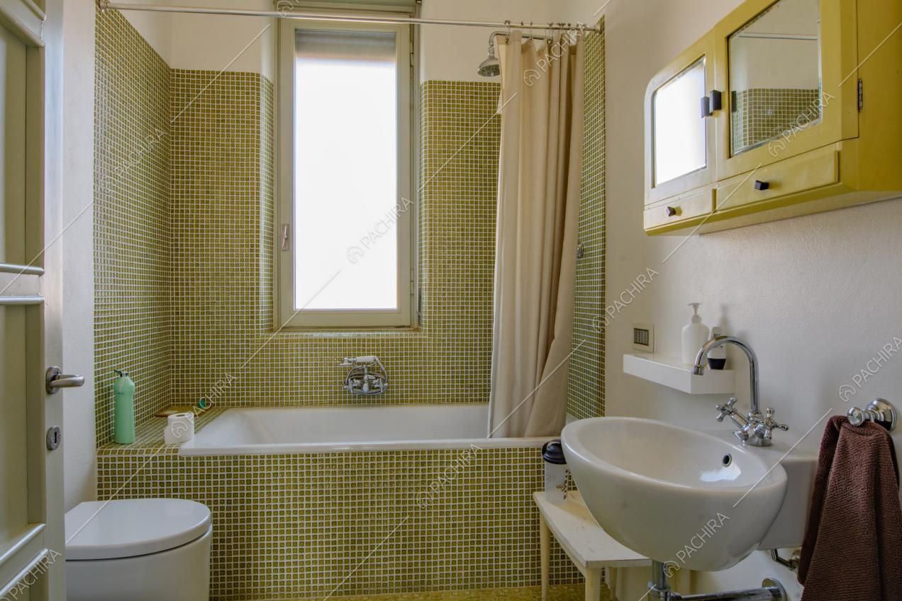Luminoso bagno con grande vasca e pareti in piccole piastrelle verdi