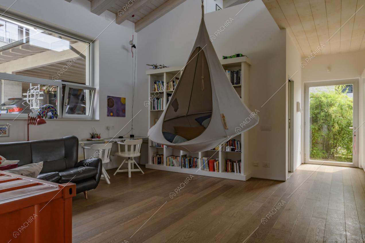 Salotto con poltrona sospesa, mobile rosso, divano nero in paelle e soffitto con travi in legno a vista