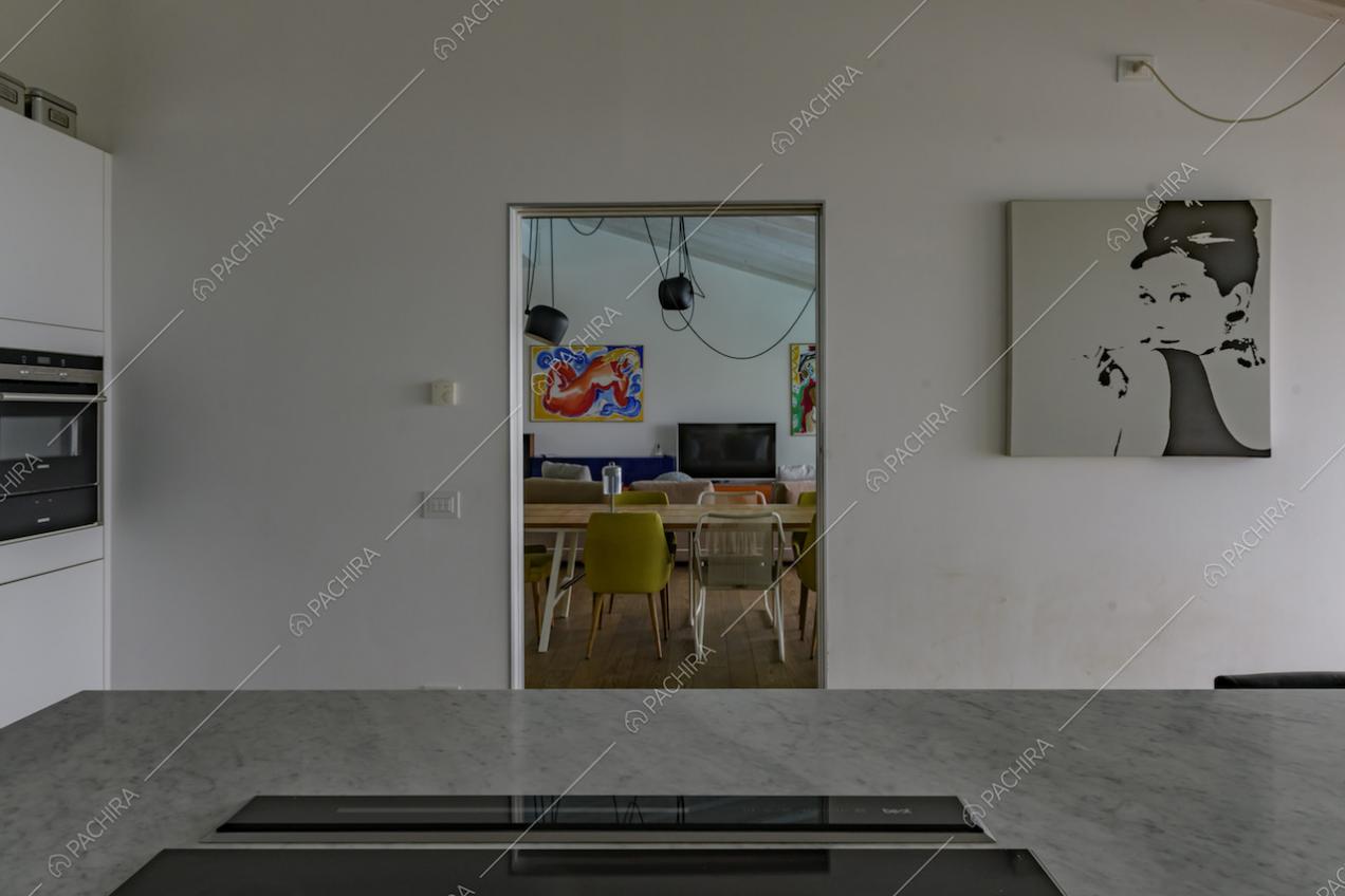 Dai fornelli a induzione sull'isola della cucina, dalle pareti bianche, vista sul tavolo da pranzo