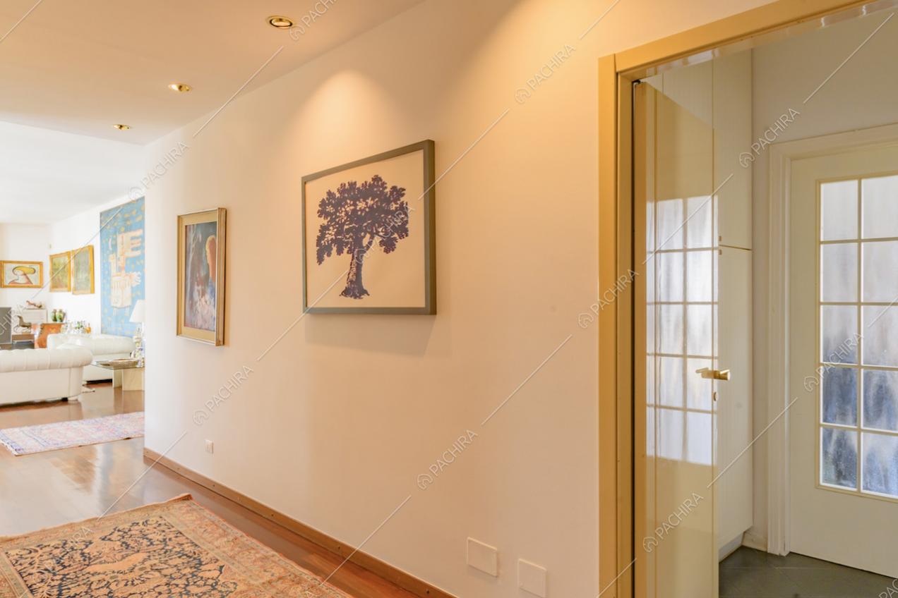 Dal corridoio con pareti bianche e pavimento in parquet vista sul soggiorno e su porta a vetri