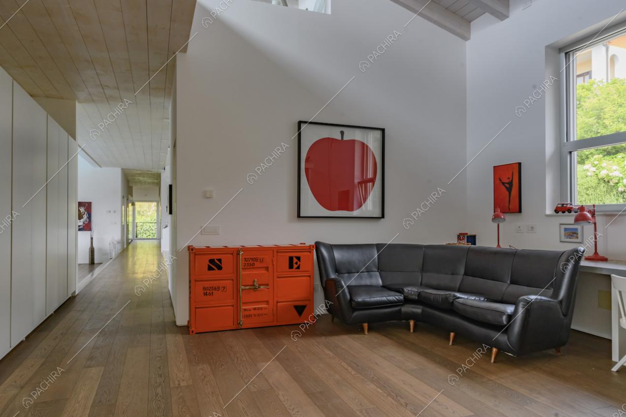 Salotto con divano nero in pelle, pareti bianche e corridoio con pavimento in parquet