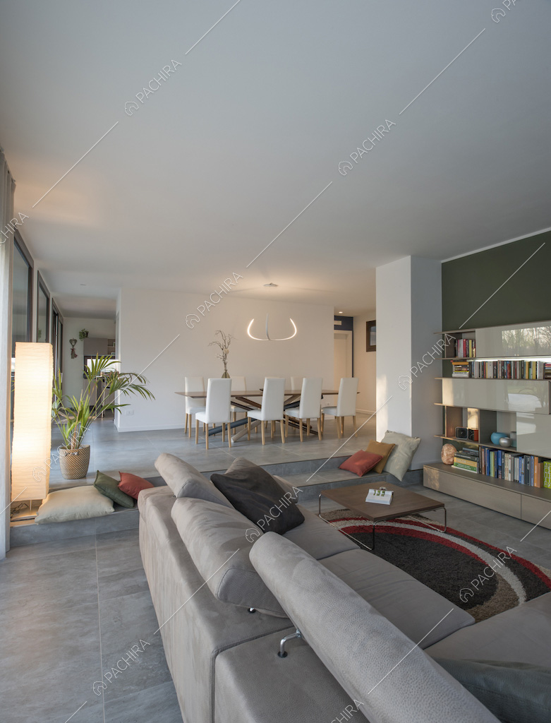 Salotto con pavimento grigio, divano e vista sul tavolo da pranzo con lampadario di design