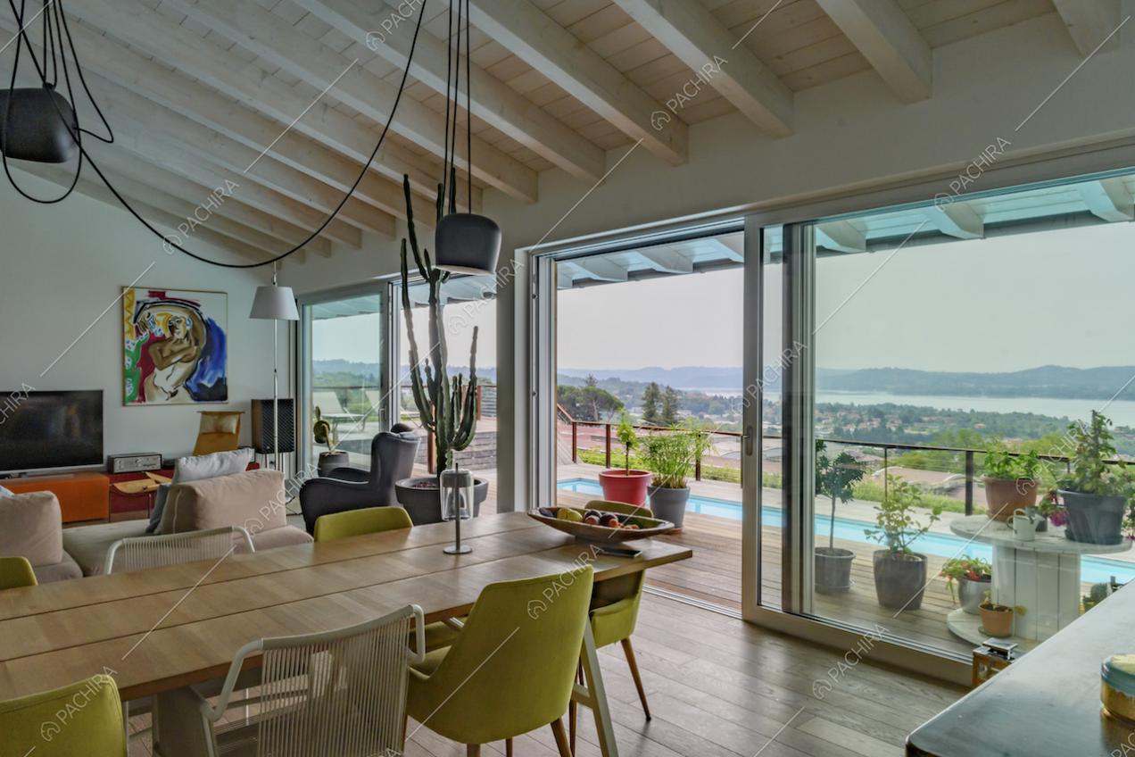 Dalla sala con soffitto in travi in legno, vista sulla terrazza con piscina e sul lago
