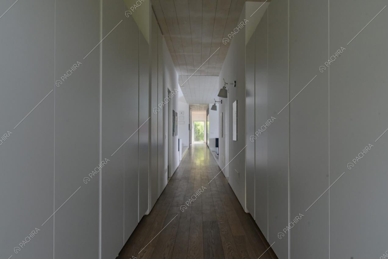 Lungo corridoio con armadi bianchi a muro, pavimento in parquet e soffitto bianco in legno