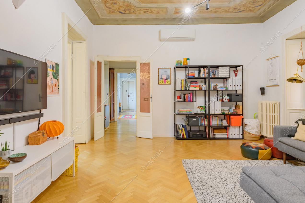 Zona living con pareti bianche, divano grigio, soffitto affrescato e vista sulla porta d'ingresso