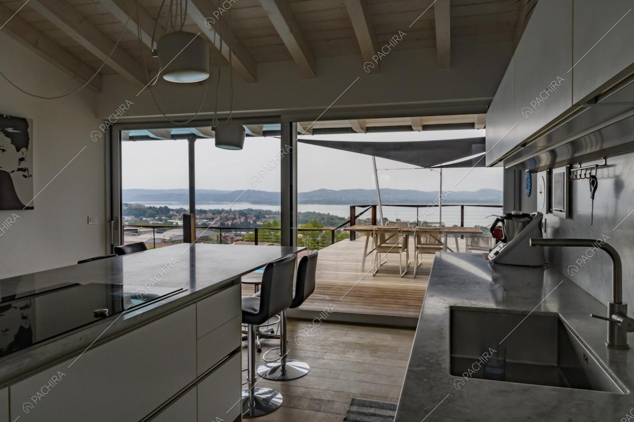 Cucina a isola con piano in marmo, fornelli a induzione, sgabelli e vista sulla terrazza tramite le vetrate