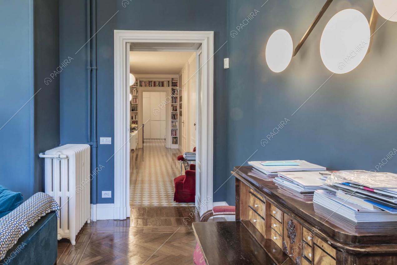 Dal salotto con pareti blu e pavimento in parquet vista sul corridoio con libreria