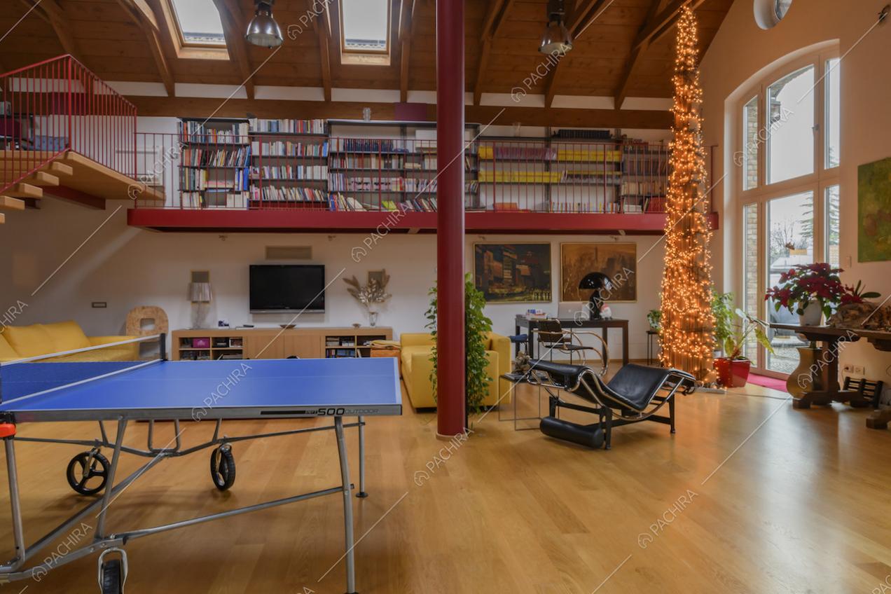 Luminoso salone con pavimento in parquet, colonna rossa e vista sulla libreria del soppalco