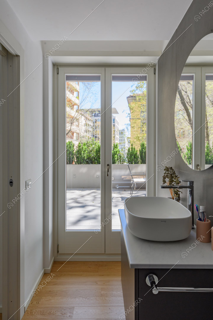 Luminoso bagno con parete grigia, pavimento in parquet e porta-finestra