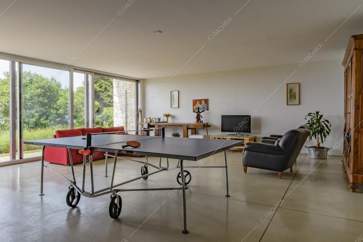 Sala con pavimento in cemento lisciato, con divani, tavolo da ping pong e pareti bianche