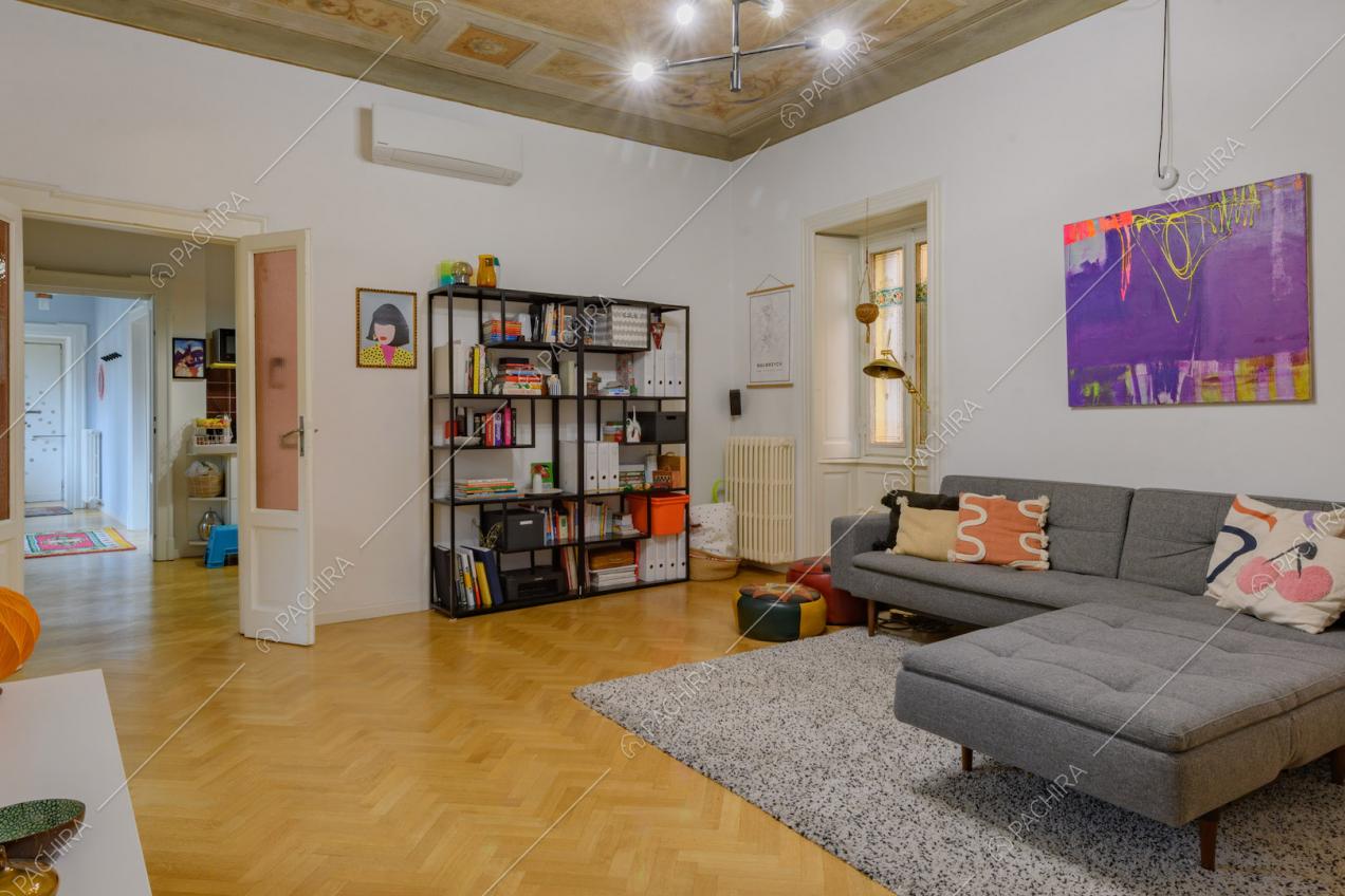 Divano grigio angolare, soffitto affrescato e pavimento in parquet a spina di pesce