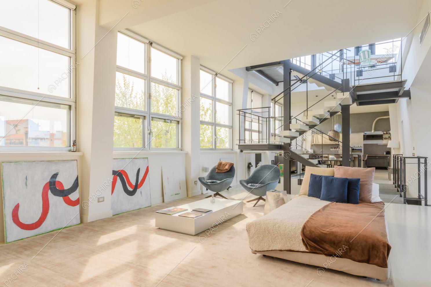 Luminosa zona living con grandi vetrate in stile industriale e vista su scale e cucina